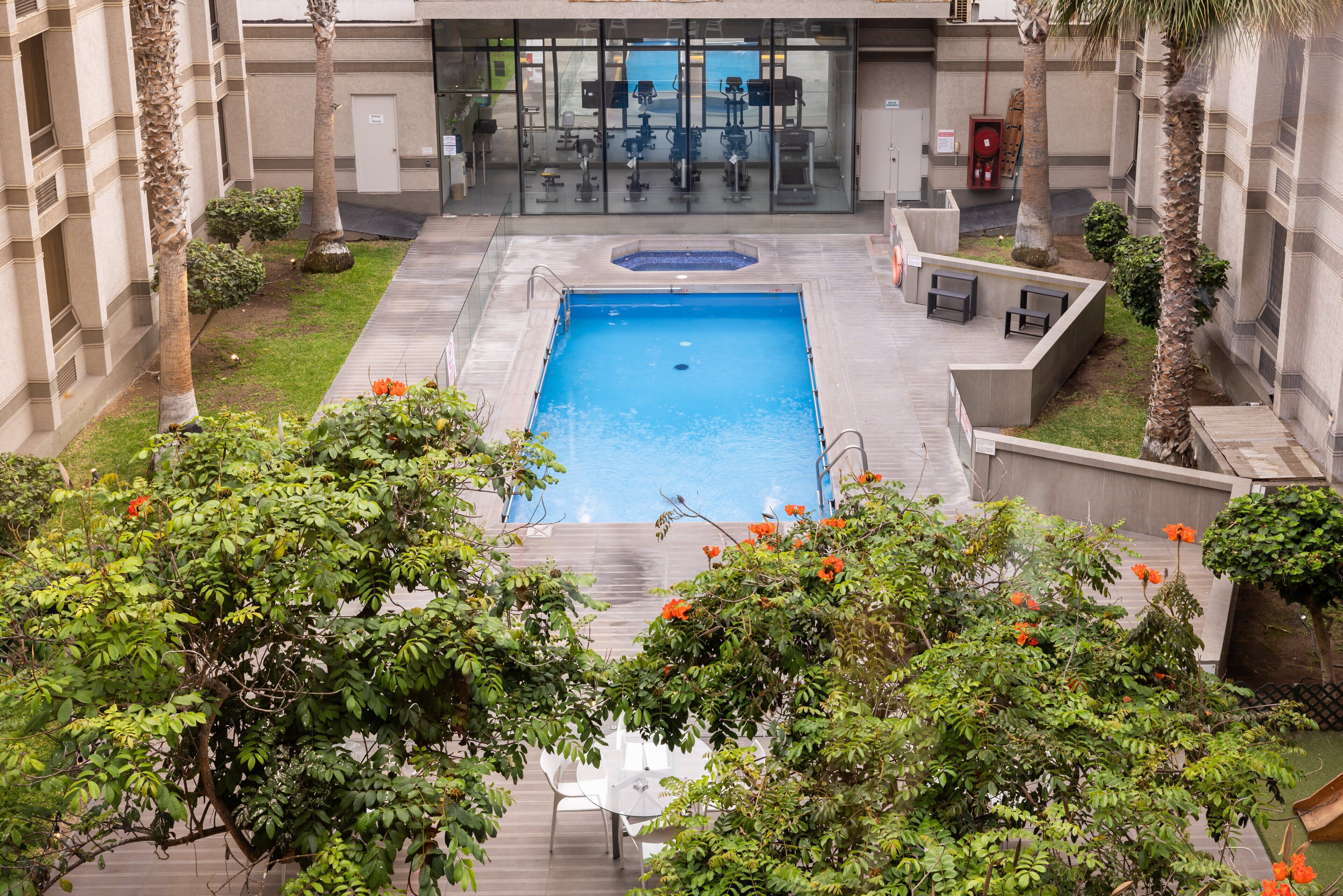 Piscina rodeada de follaje y equipo de ejercicios.
