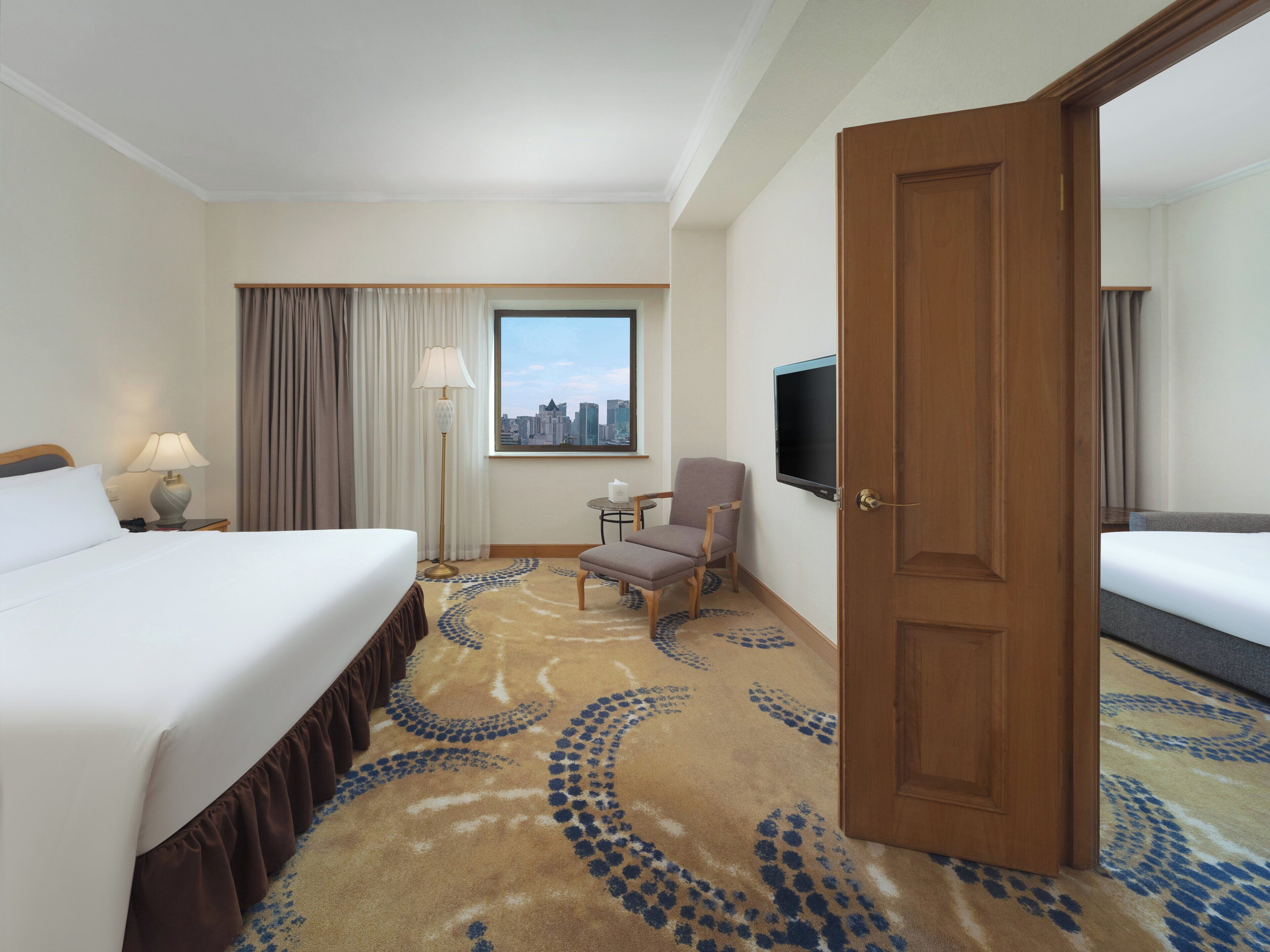 Une chambre d’hôtel équipée d’un lit, d’une chaise, d’un bureau, d’une lampe, d’une télévision et offrant une vue sur le panorama urbain.