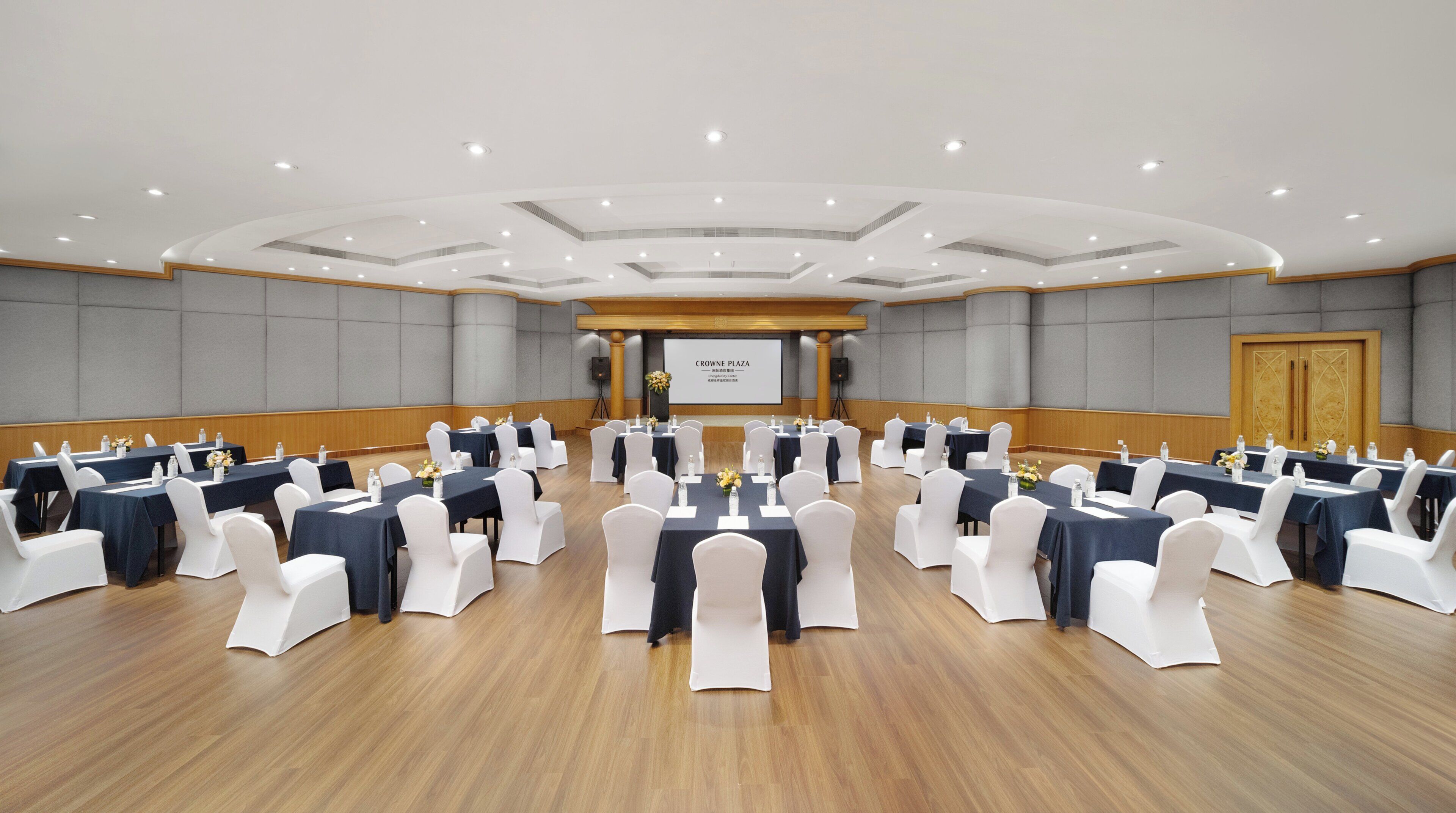 Une salle de conférence avec des tables rondes, des chaises blanches et un écran de présentation.