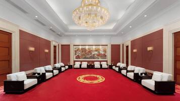 A conference room with a red carpet, white chairs, a large chandelier, and a painting on the wall.