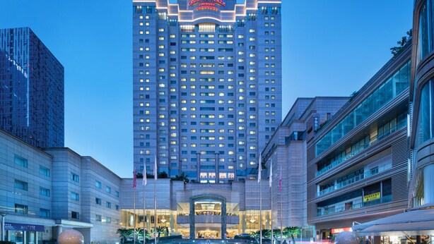 Un hotel moderno de gran altura con un cartel llamativo en la parte superior, varios pisos y una entrada bien iluminada.