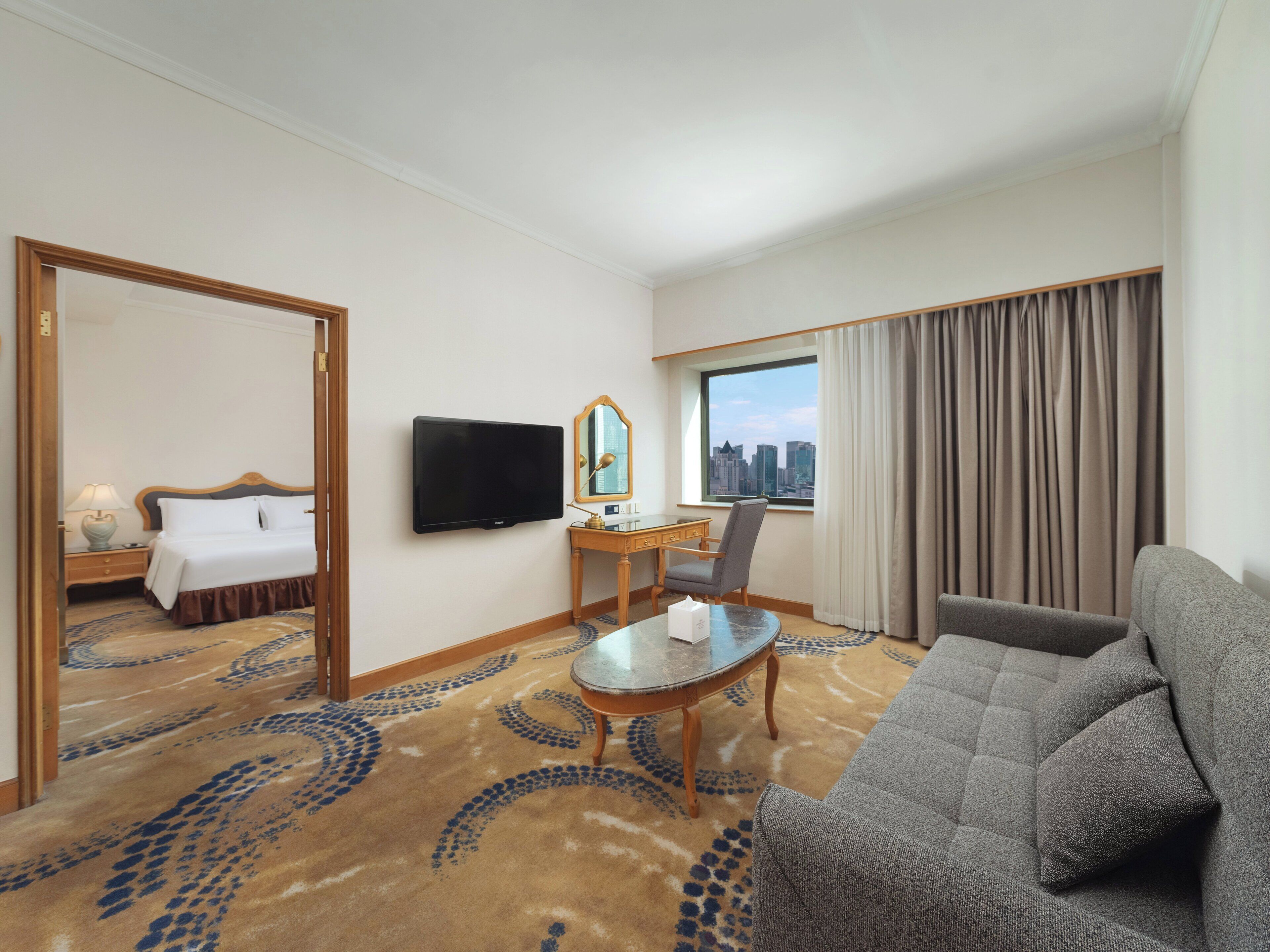 Habitación de hotel con cama, escritorio, silla, sofá, televisor y vista de la ciudad.