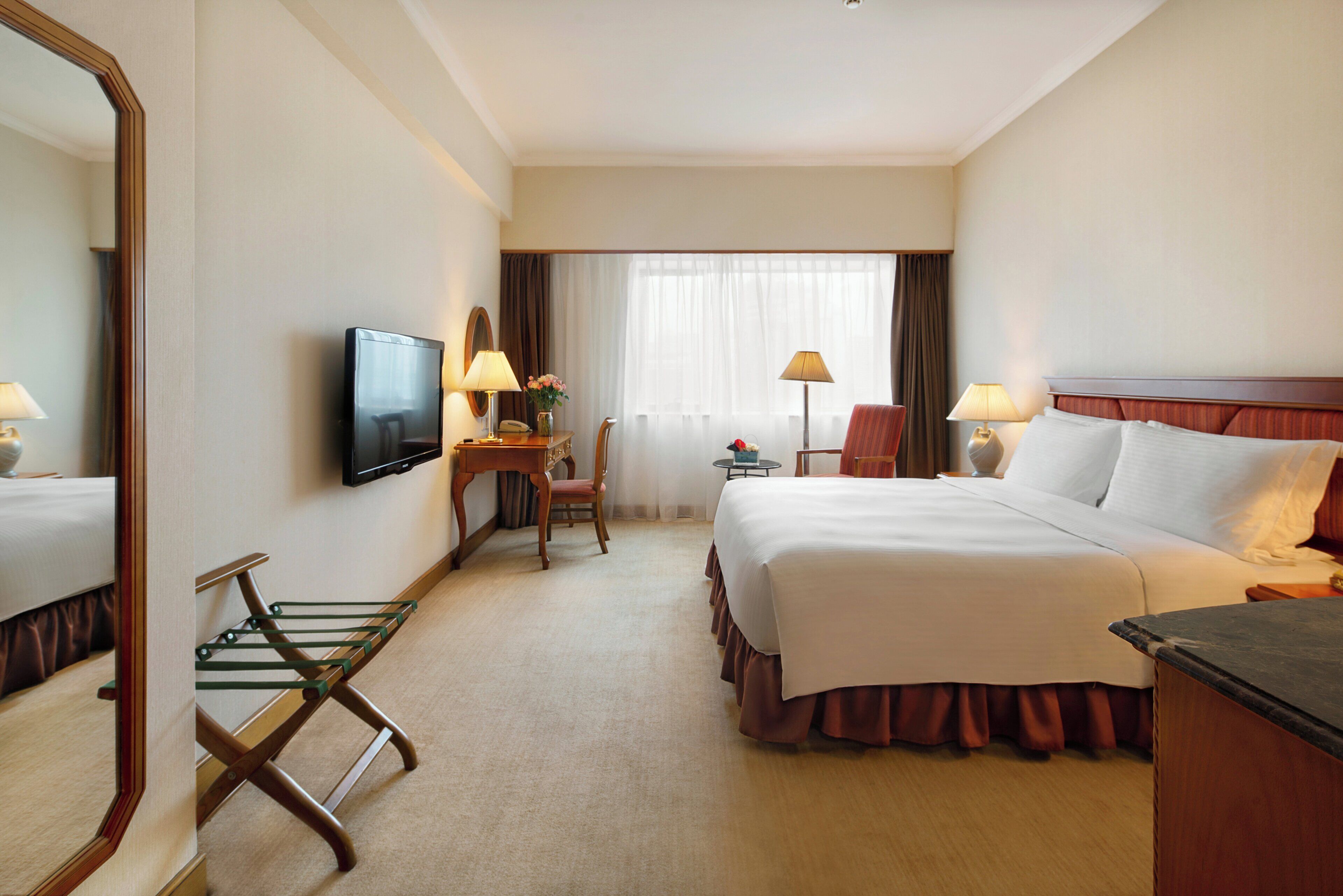 Habitación de hotel con cama, escritorio con silla, televisión, lámpara y espejo.