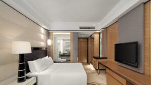 Una habitación de hotel moderna con una cama grande, un televisor de pantalla plana, una mesita de noche con lámpara y una mesa de centro de vidrio.