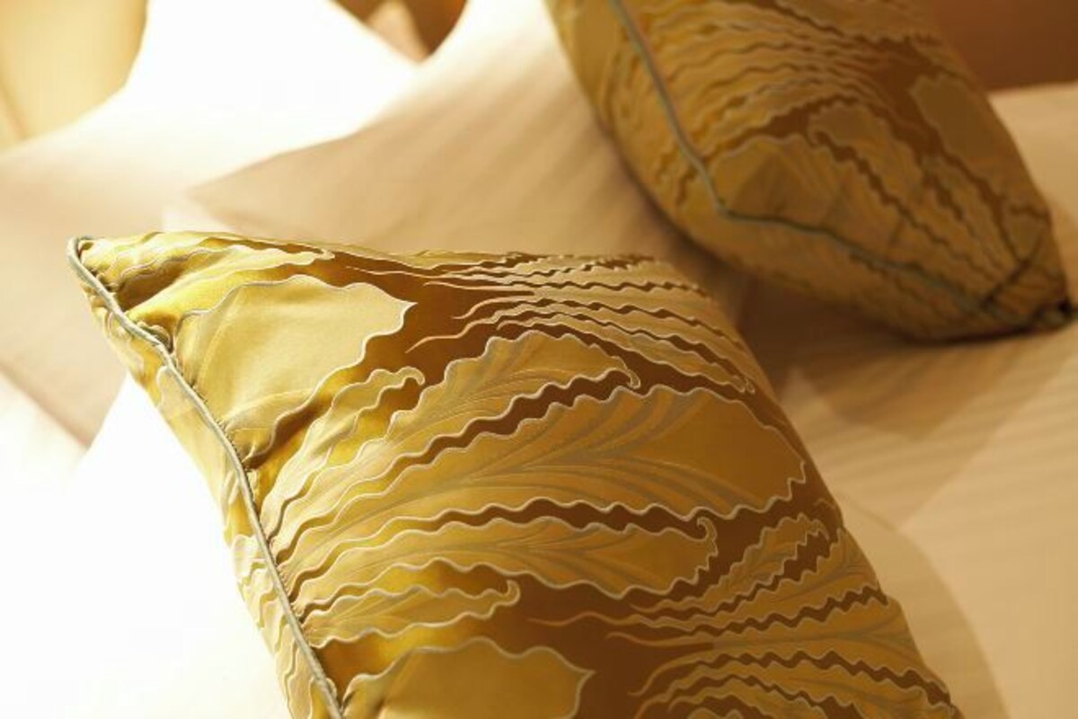 A bed with a white sheet and two pillows with a leaf pattern.