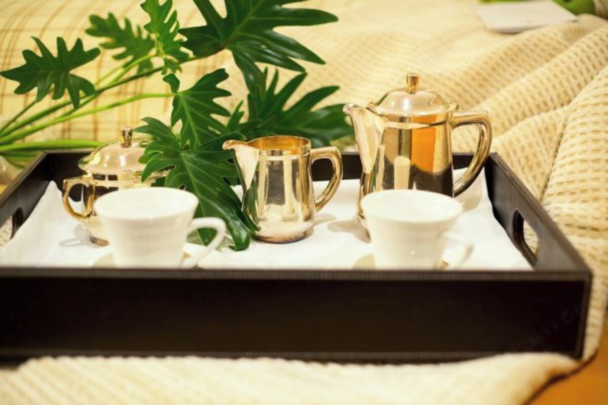 A tray with a teapot, two cups, and a sugar bowl, accompanied by green leaves, on a textured surface.