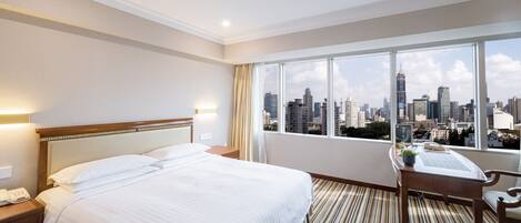Habitación de hotel con una cama grande, un escritorio y vistas a un horizonte urbano.
