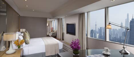 Ein modernes Hotelzimmer mit einem großen Bett, einem Schreibtisch mit Lampe, einer Vase mit Blumen und Blick auf die Skyline der Stadt.