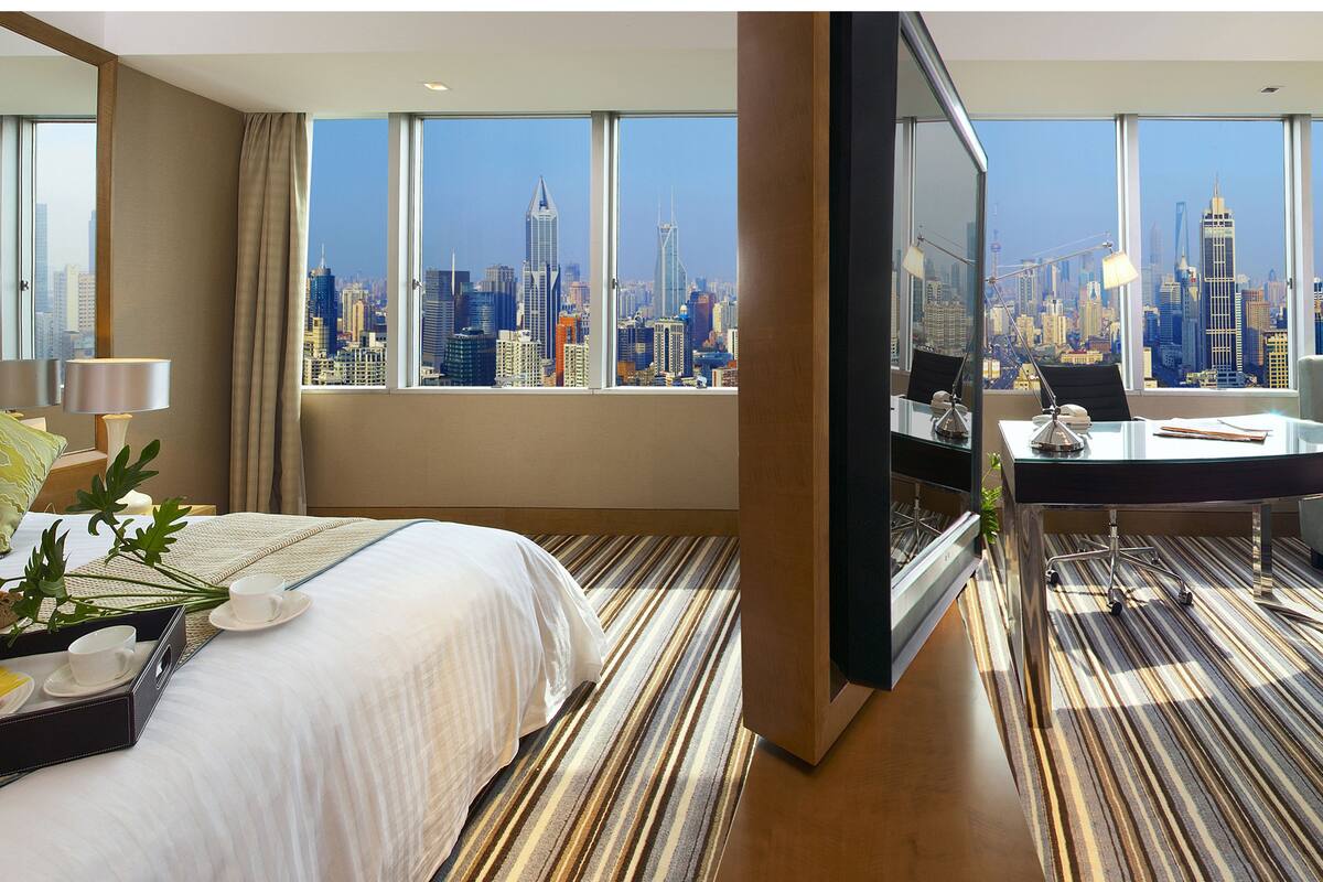A hotel room with a large bed, a desk with a computer, and a view of a city skyline.
