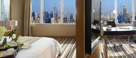 A hotel room with a large bed, a desk with a computer, and a view of a city skyline.
