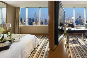 Habitación de hotel con una cama grande, un escritorio con computadora y vistas a un horizonte urbano.