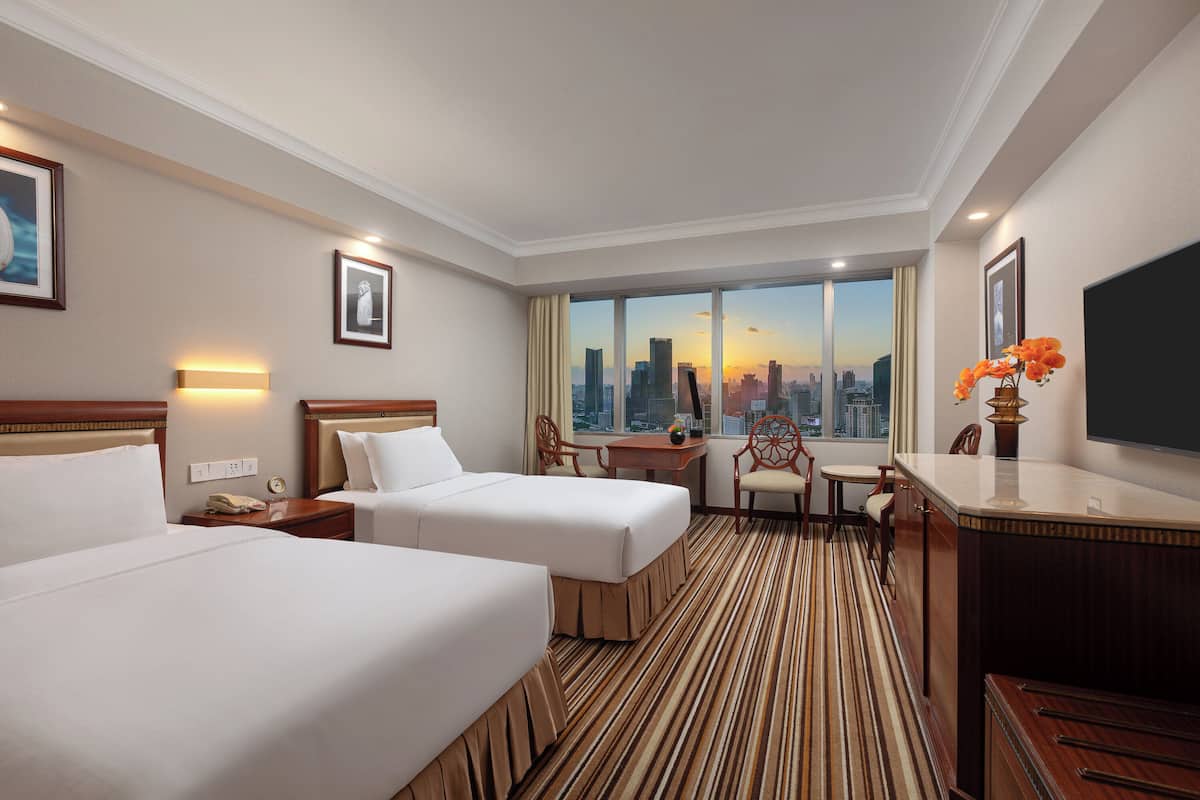 A hotel room with two beds, a desk, a chair, a television, and a large window with a city view.