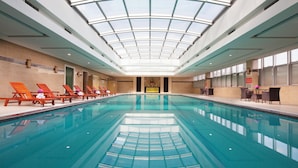 Una piscina interior con techo de cristal, sillas de descanso y una zona de recepción.
