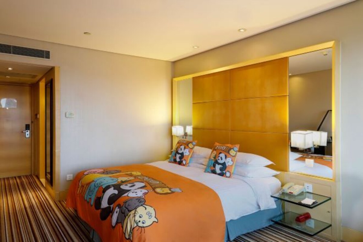 A hotel room with a bed, a bedside table with a lamp, a large mirror, and a striped carpet.