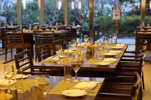 A restaurant with multiple dining tables set with white tablecloths, wine glasses, and neatly folded napkins.