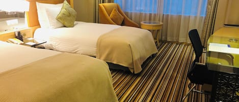 A hotel room with two beds, a small round table, a chair, and a desk with a computer.