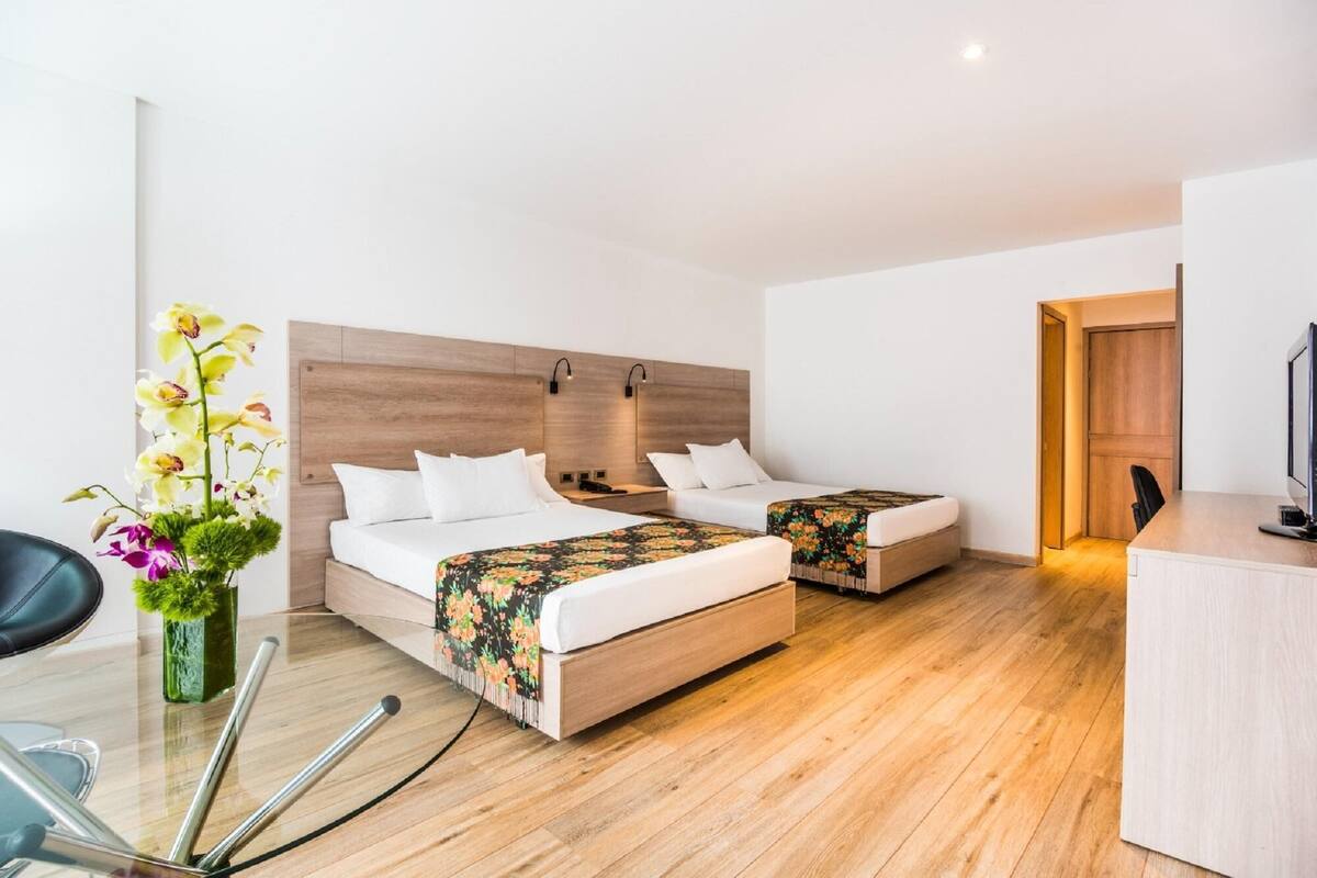 Une chambre d’hôtel avec deux lits, un bureau, une chaise et un vase avec des fleurs.