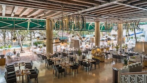A spacious indoor dining area with multiple tables and chairs, a pool visible through large windows, and a rustic ceiling with exposed beams. - Las Americas Casa de Playa (Cartagena)