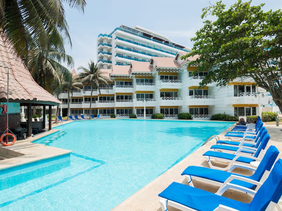 Un hôtel doté d’une piscine, de chaises longues bleues et d’un palmier.