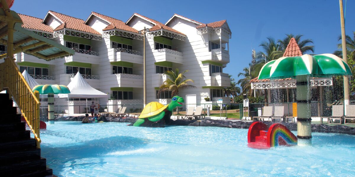 A swimming pool with a water slide, inflatable toys, and a building with balconies in the background.