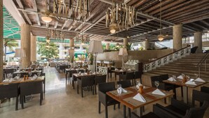 A spacious restaurant with high ceilings, exposed beams, and hanging light fixtures. Tables are set with white tablecloths and wine glasses. - Las Americas Casa de Playa (Cartagena)
