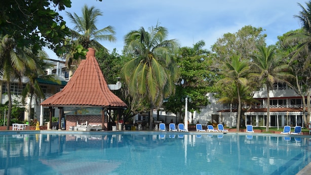 A swimming pool with blue lounge chairs, a gazebo, and palm trees. - Las Americas Casa de Playa (Cartagena)