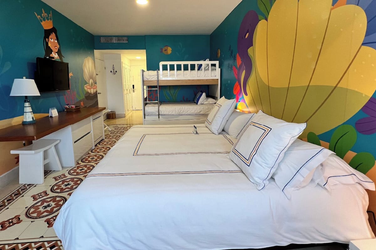 A hotel room with a bunk bed, a desk with a lamp, and a colorful mural on the wall.