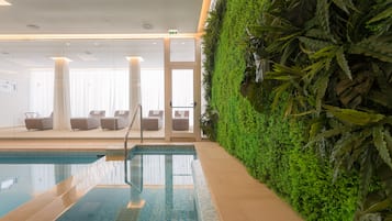 A swimming pool with a glass wall, a seating area with chairs, and a green wall with plants.