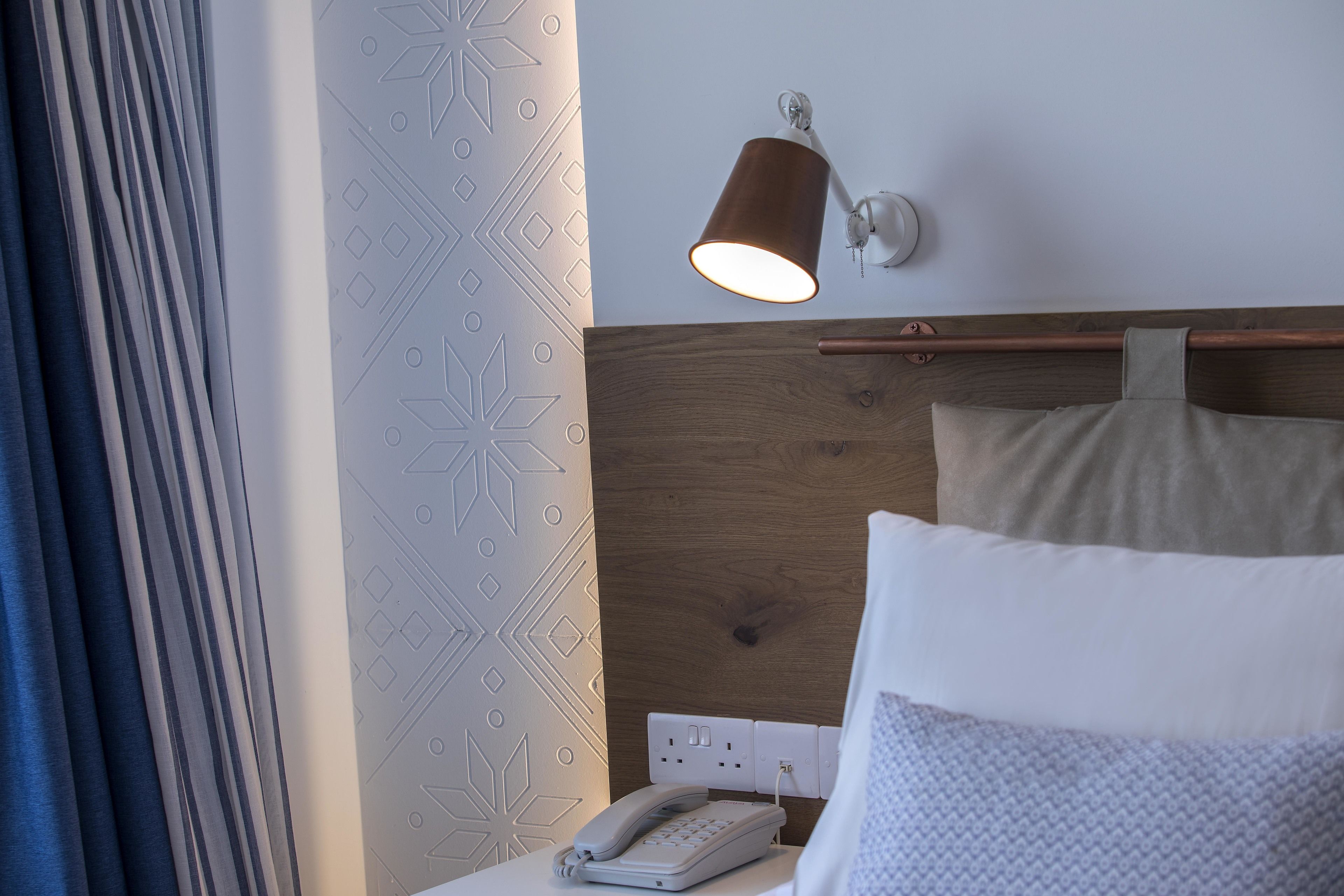 A hotel room with a bed, a bedside table with a lamp, and a wall-mounted phone.