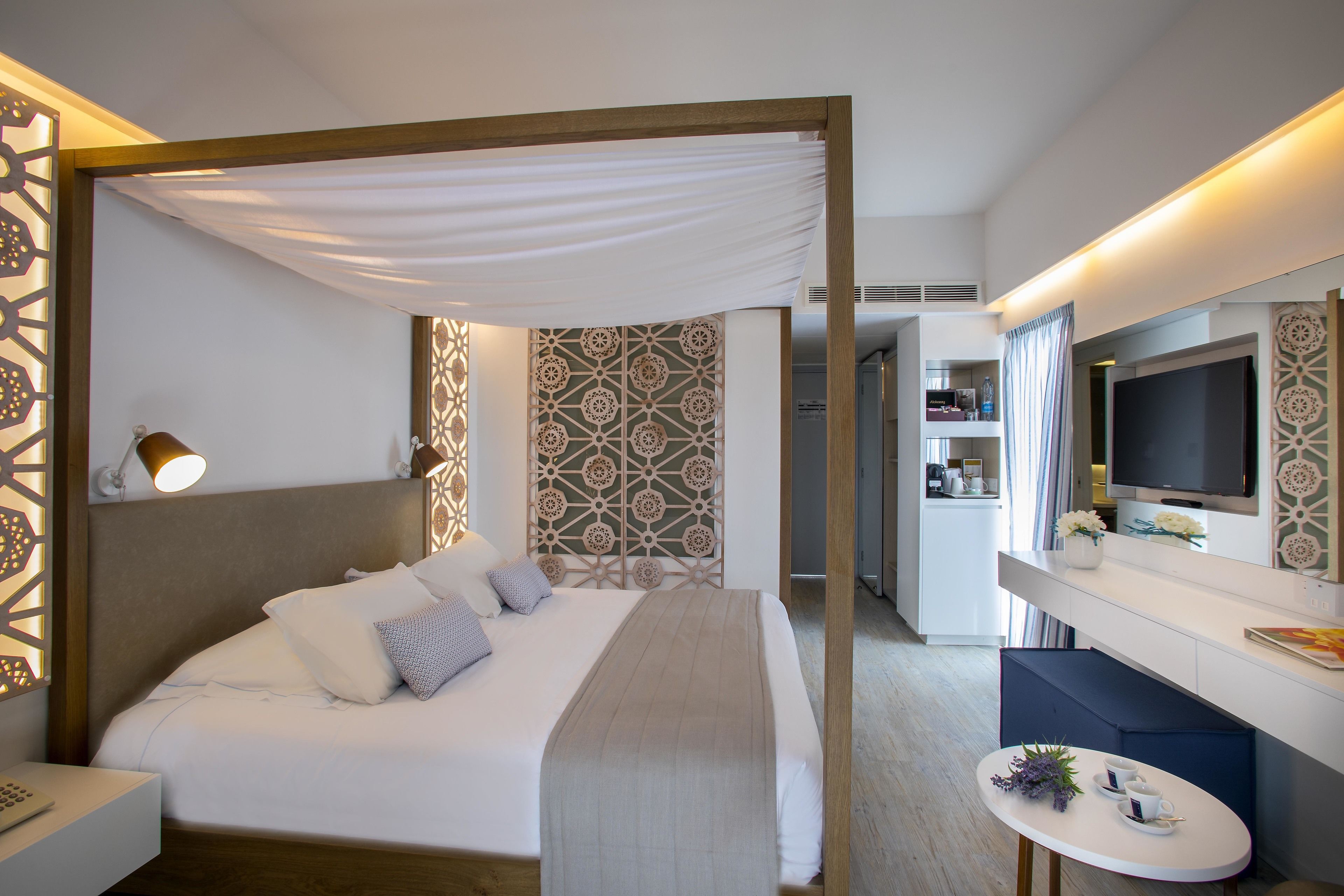 Una camera d'albergo con un letto, un comodino, una televisione e un tavolino con un vaso e dei fiori.