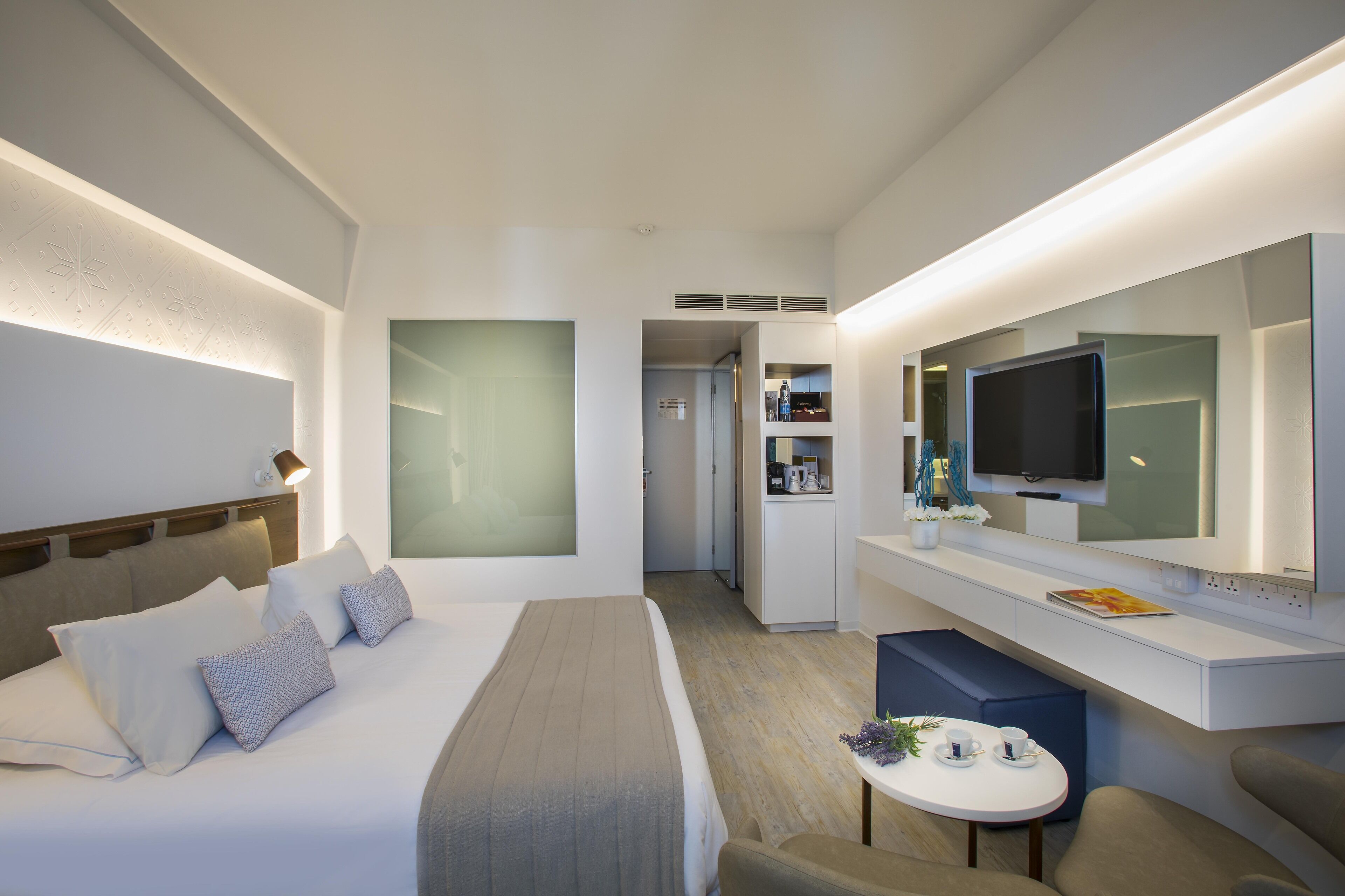 A modern hotel room with a large bed, a desk, a television, and a small seating area.