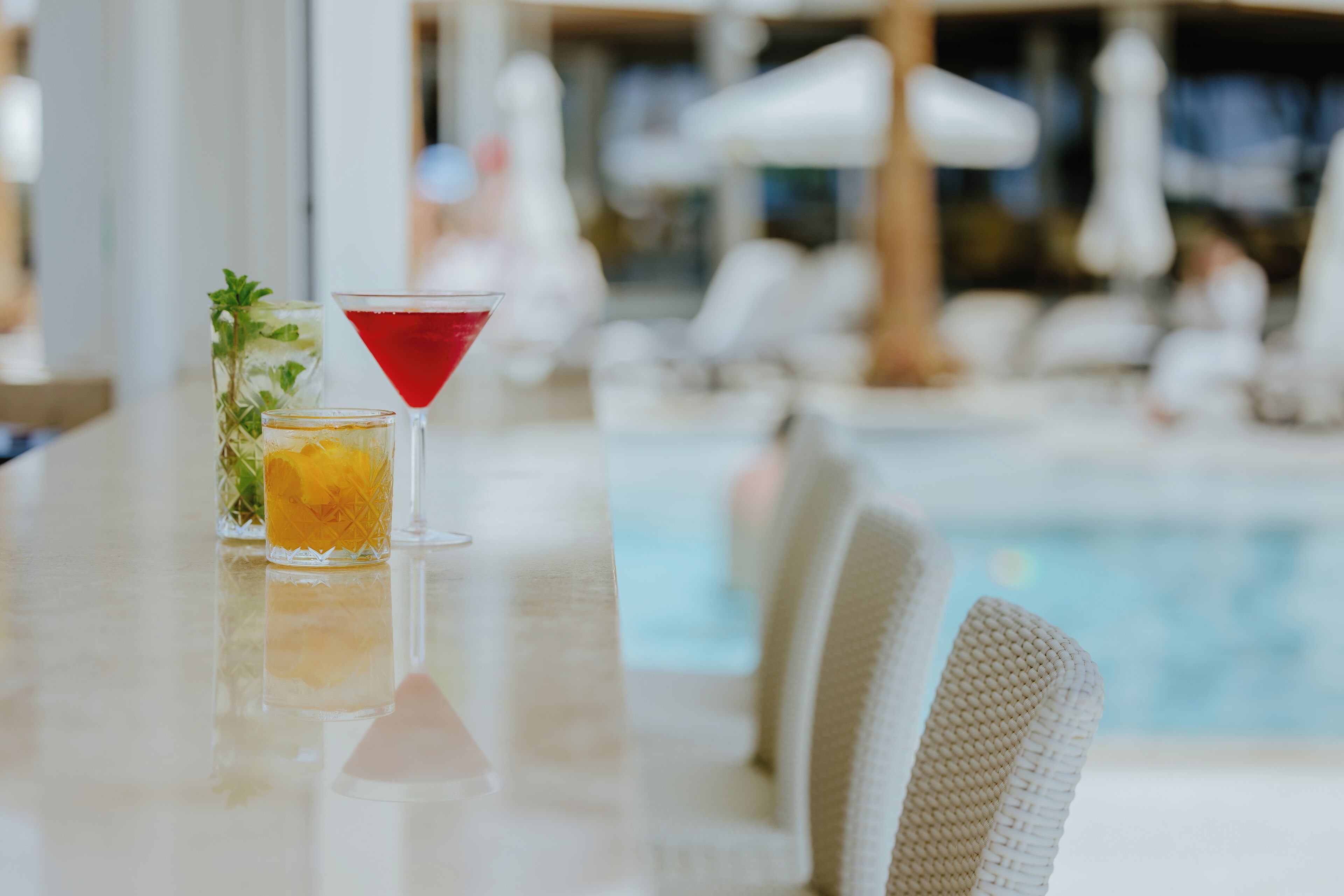 A poolside bar with two drinks, a glass with a yellow drink, and a martini glass with a red drink.