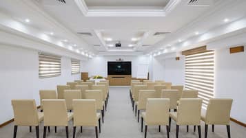 A conference room with rows of beige chairs, a podium, and a projector screen.