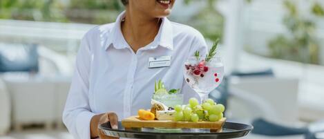 A person holding a tray with a drink, grapes, and a cheese board.