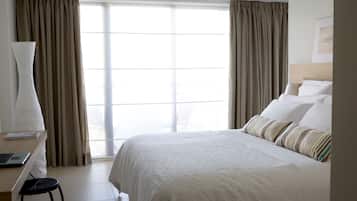 Una habitación de hotel con una cama grande, un escritorio con una computadora portátil, una silla y una ventana con cortinas.