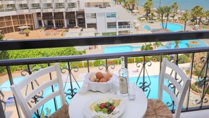A balcony with a table set for dining, overlooking a pool and a hotel building.