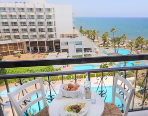 A balcony with a table set for dining, overlooking a pool and a hotel building.
