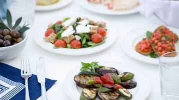 Una mesa servida con diversos platos, incluyendo una ensalada, verduras a la parrilla y pan, con un tenedor y un cuchillo a la izquierda.