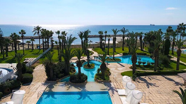 A resort with a large pool, palm trees, and a view of the sea.
