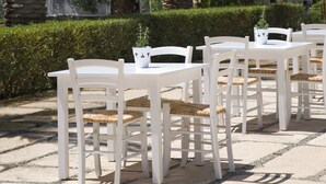 Outdoor seating with white tables and chairs, surrounded by palm trees and a stone wall.