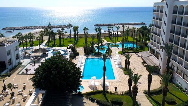 A resort with a large central pool, a smaller pool, and a beach area with palm trees.