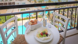 A balcony with a table set for a meal, overlooking a pool and a beach.