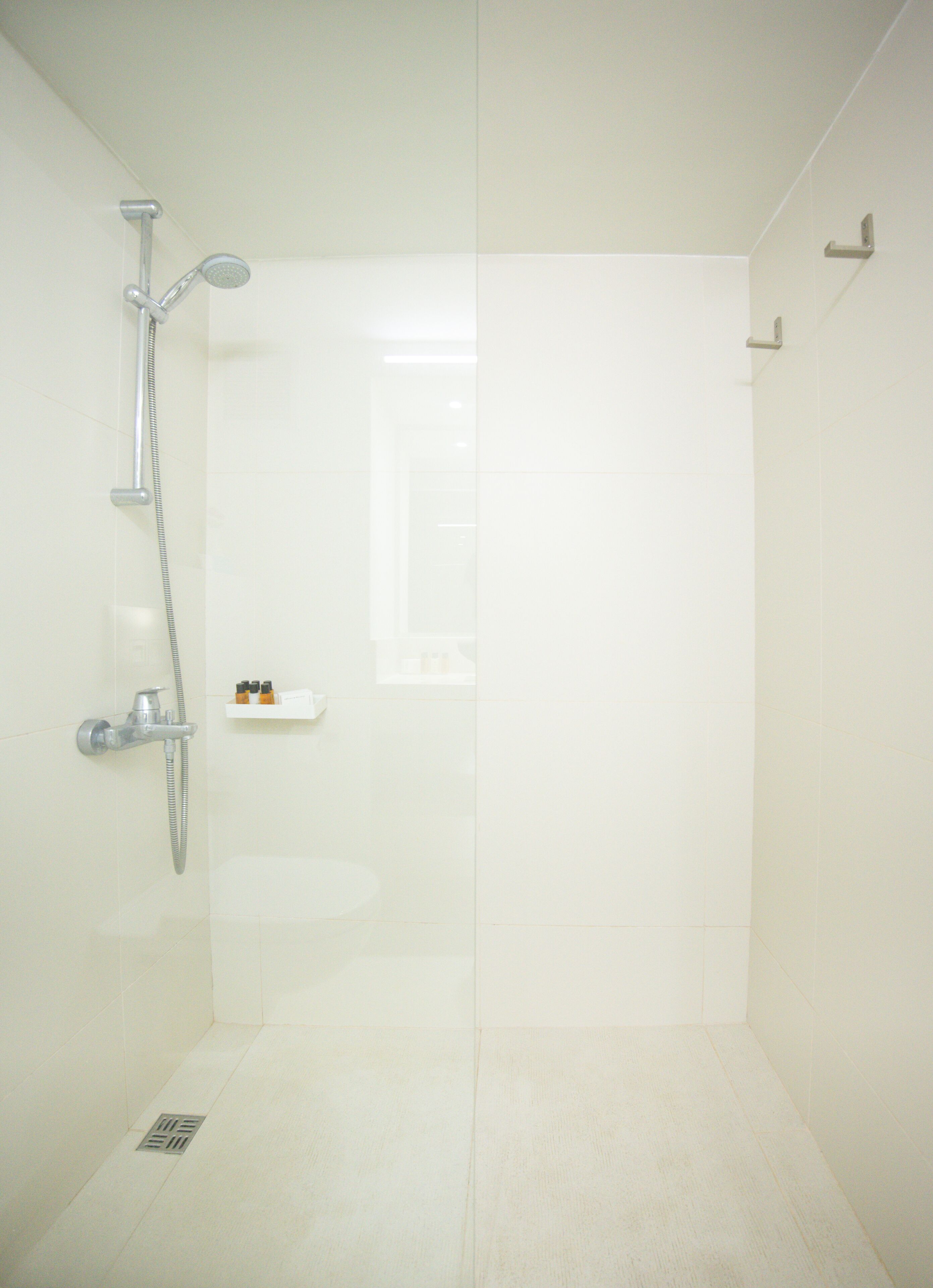 Un baño moderno con cabina de ducha de vidrio, ducha de mano y una pequeña repisa con artículos de aseo.