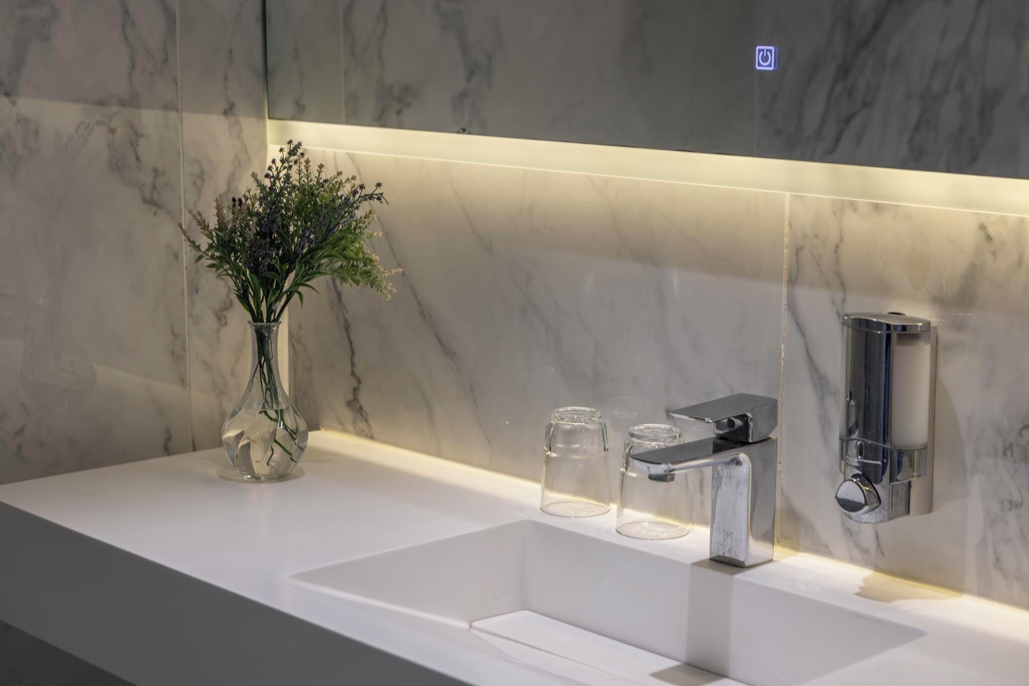 A modern bathroom with a white sink, a glass vase with flowers, and a wall-mounted faucet.