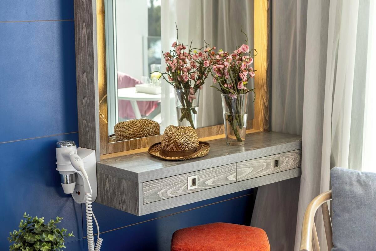 A bathroom vanity with a mirror, two vases with pink flowers, a hairdryer, and a woven basket.