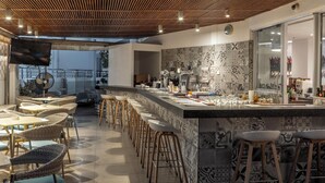 A modern bar area with a long counter, bar stools, and a television screen. - Park Beach Hotel (Limassol)