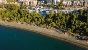 An aerial view of a coastal area with modern buildings, a beach, and dense greenery. - Park Beach Hotel (Limassol)