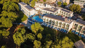 An aerial view of a hotel with multiple buildings, a swimming pool, and surrounding greenery. - Park Beach Hotel (Limassol)