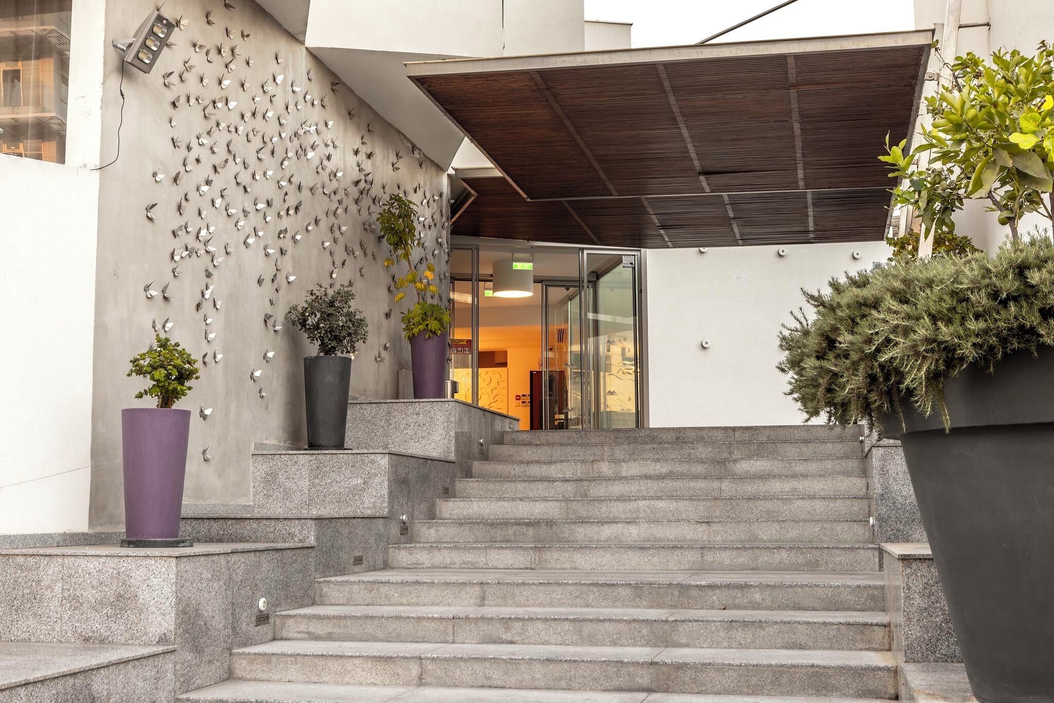 A modern building entrance with a concrete wall decorated with metallic elements and potted plants.