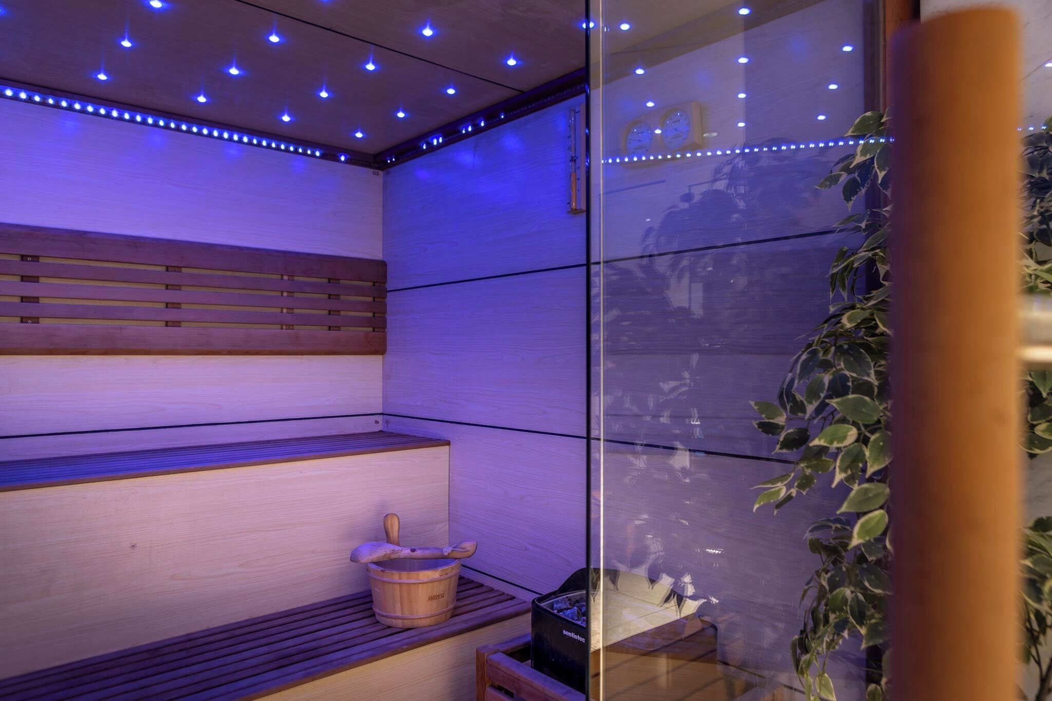 A sauna with wooden benches, a wooden bucket, and a glass enclosure.